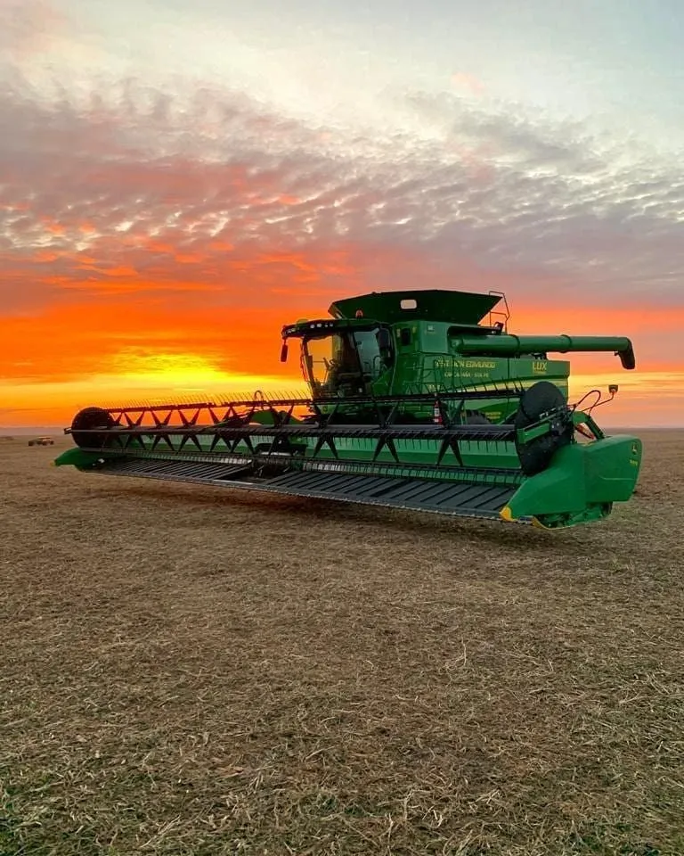 Colheitadeira verde parada na lavoura ao pôr do sol