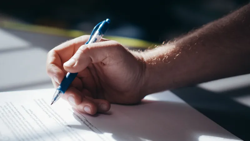 Mão assinando um documento com uma caneta