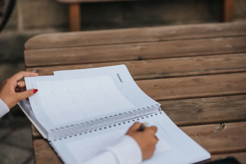 Mãos anotando um planejamento em um caderno sobre uma mesa de madeira