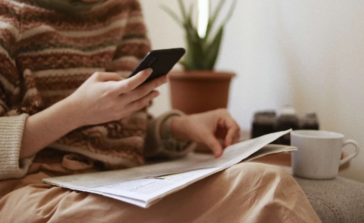Pessoa usando o celular com papéis nas mãos